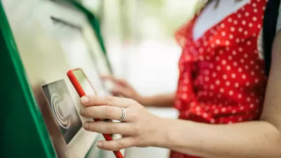 Close-up of woman holding up smartphone up to contactless public transit payment kiosk