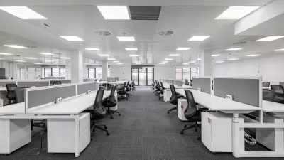 Large empty open-plan office with rows of white desks and black chairs under bright fluorescent lighting