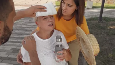 Two people helping an older woman outdoors suffering from heat stroke.