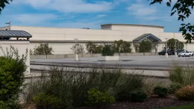 Large blank mall building with only two cars in large parking lot.