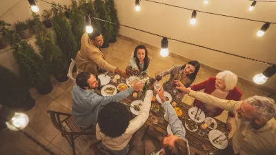 Diverse group of people sitting around a table doing a toast on a patio with warm bistro lights.