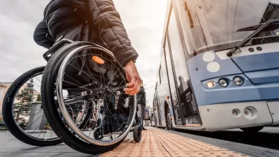 Ground-up view of man using wheelchair waiting to board a light blue bus.