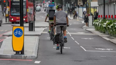 Protected two-way cycletrack on street in London, UK with red double-decker bus in background.