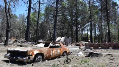 Burned car sits in front of burned house in forest in Paradise, California after the Camp Fire.