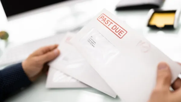 Close-up of hand holding white envelope with red "Past Due" stamp.