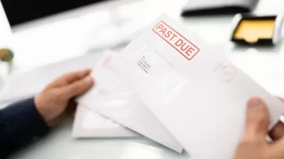 Close-up of hand holding white envelope with red "Past Due" stamp.