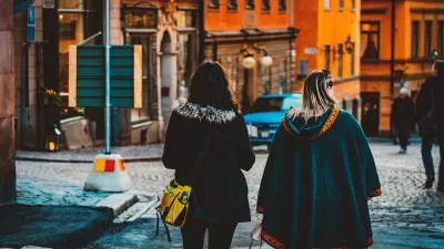 View from back of two women in winter clothing walking down street in European city.