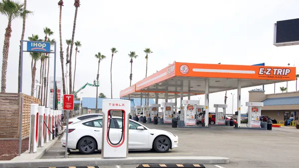 E-Z Trip gas station in Bakersfield, California with orange awning over regular gas pumps and Tesla superchargers with white Teslas charging in foreground.