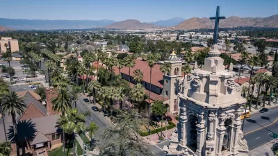Aerial view of Riverside, California with ornate Catholic church tower in foreground and mountains in the distance.