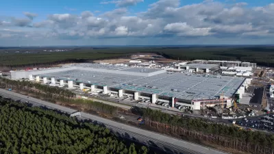 Birds-eye view of a large EV factory and nearby highway, all surrounded by forest.
