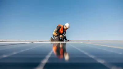 Worker in safety vest and white hard hat installing rooftop solar panel.
