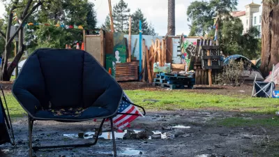 Empty navy blue camping chair with small American flag in front of unhoused encampment in People's Park, Berkeley, California.