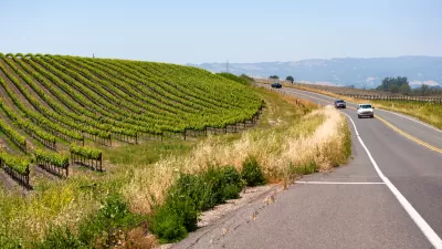 View of two trucks on asphalt two-lane road in Vapa Valley with vineyards along side of road