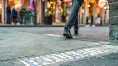 Low close-up of tile BOURBON sign in New Orleans street with pedestrian walking in background.