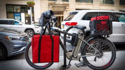 Black e-bike with red food delivery bags locked at bike rack on New York City street.