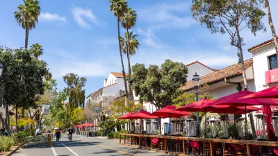 View of Santa Barbara, California street with neo-Spanish colonial architecture and wooden outdoor dining deck with tables and red umbrellas.