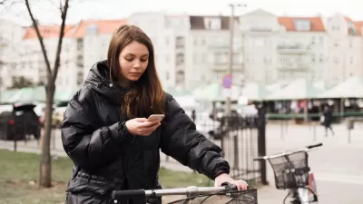 Woman stands next to a bike with one hand on handlebar holding her mobile phone.
