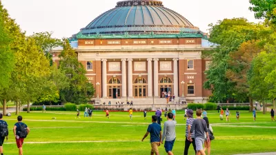 College students walking on green lawn with neoclassical red brick domed building in background on University of Illinois campus.