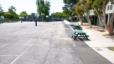 View of empty paved schoolyard with green picnic benches and basketball hoops in Malibu, California