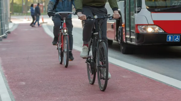 Two people on bikes in red painted bike lane with bus in traffic lane next to them.