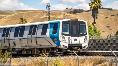 A white and blue Bay Area Rapid Transit (BART) train with golden hills and a palm tree in background.