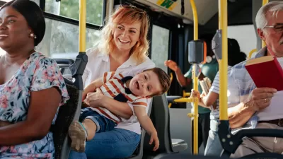 Woma holding small boy on lap sitting on public bus with many other passengers around them.