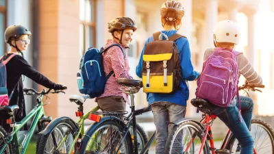 Group of four children with backpacks and helmets riding and walking their bikes.