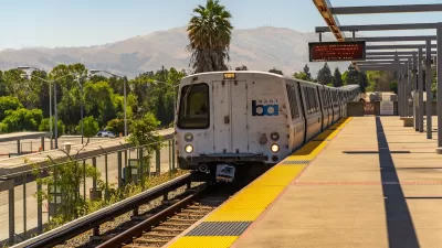 San Francisco Bay Area Rapid Transit train at elevated station with hills and palm tree in background.
