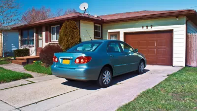 Blue small sedan in driveway of ranch-style one-story home with light green walls and dark brown garage door and trim.