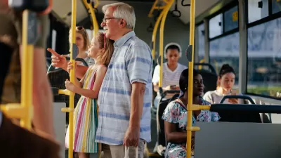 Elderly man and granddaughter standing on public bus.