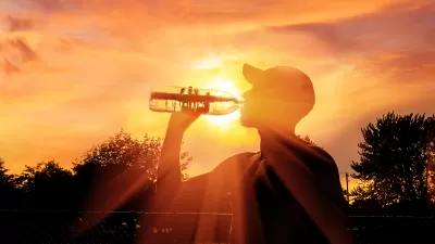 Man drinking water from plastic bottle sillhouetted against orange sky signaling extreme heat