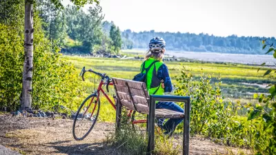 Cyclist in helmet sitting on bech looking out at lake and forest in Anchorage, Alaska.