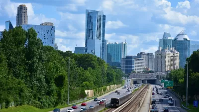 MARTA train tracks run in the middle of a six lane highway with an overpass and the Buckhead city skyline of skyscrapers in the background.