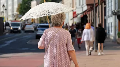 Older woman walking on city street holding white lace sun parasol.