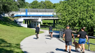 Concrete bike and pedestrian trail with people walking and biking under pedestrian bridge in Orlando, Florida.