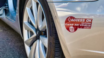 Close-up of maroon California 'Clean Air Vehicle' carpool lane access sticker on the back bumper of a silver Tesla vehicle.
