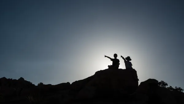 Two children sitting on rock sillhouetted against sky.