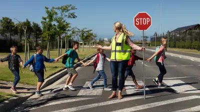 Group of children crossing a street with a crossing guard holding up red Stop sign.