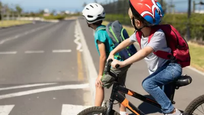 Two young boys wearing bike helmets looking right before crossing the street on their bicycles