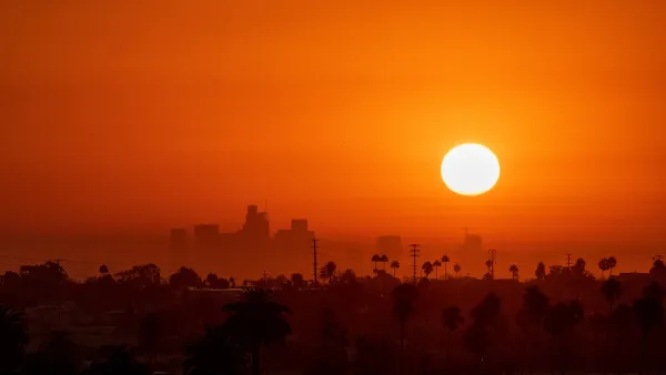 Sun rising over downtown Los Angeles with tall palm trees visible in foreground. Image is bright orange-red indicating extreme heat.