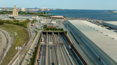 Aerial view of an eight-lane highway tunnel with the harbor in the background.