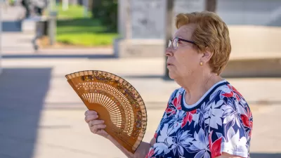 Older woman with short hair fanning herself with wood hand-held fan outdoors during hot afternoon