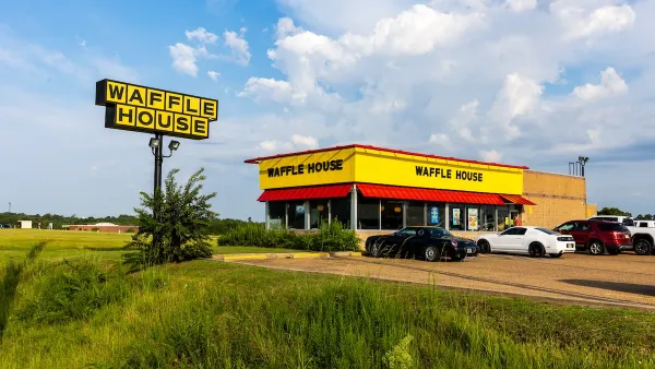 Waffle House restaurant in rural open area with large yellow and black sign and several cars parked in front.