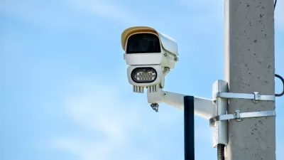 Close-up of white traffic enforcement camera mounted on concrete pole against blue sky.