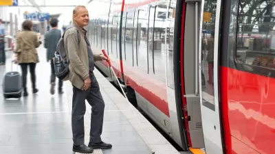 Man using cane for visual impairment waiting to board subway train on platform.