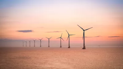 Row of offshore wind turbines in large water body against sunrise or sunset sky.