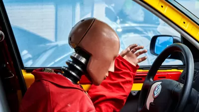 Close-up of crash test dummy in orange jumpsuit leaning over steering wheel with Volkswagen logo.
