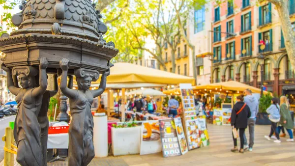 Close-up of decorative water fountain on La Rambla pedestrian street in Barcelona, Spain with blurred pedestrians in background.