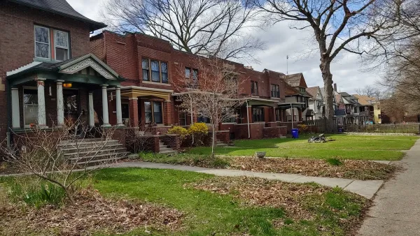 Row of older brick houses in Detroit with front porches and front lawns.