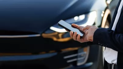 Close-up of hand holding smartphone and Tesla car hood in background.